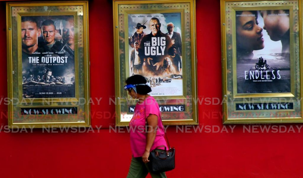 In this September 16, 2020, a woman walks past movie posters at MovieTowne, Mucurapo. Cinemas can open and sell food and drinks the Prime Minister announced on Saturday. - SUREASH CHOLAI