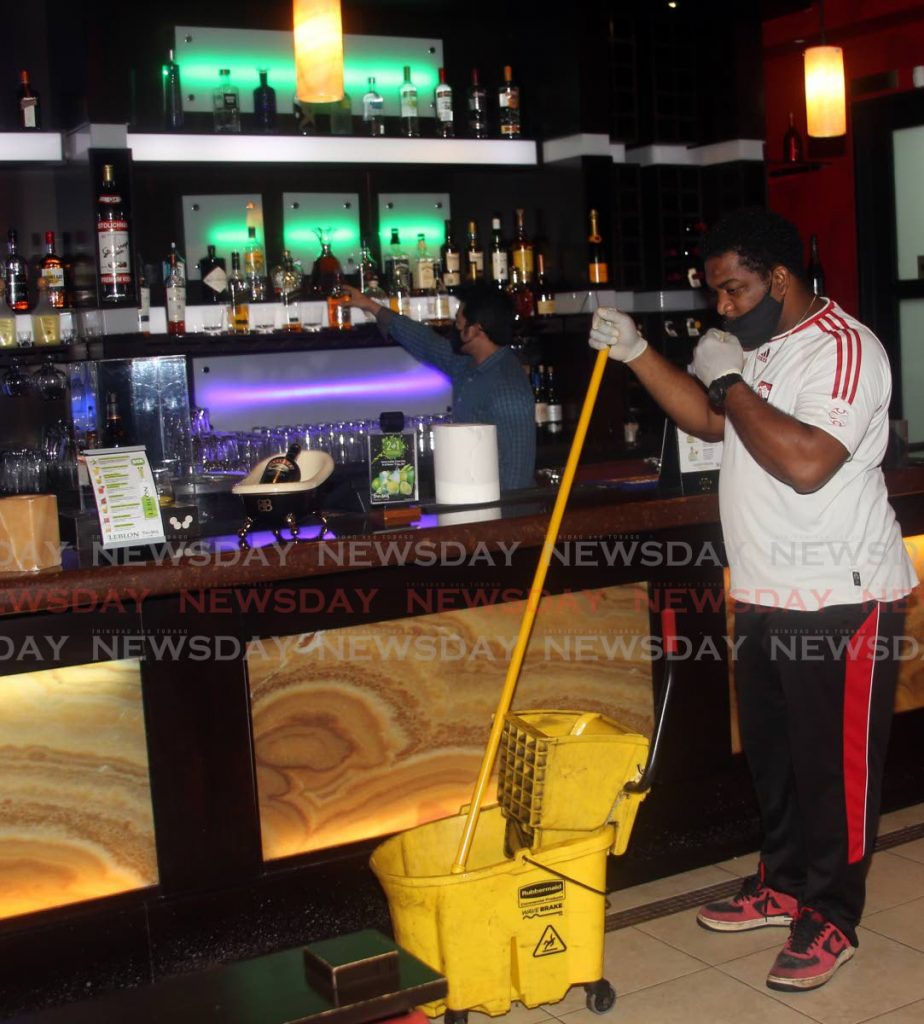 FILE PHOTO: An employee at Texas de Brazil restaurant in MovieTowne, Port of Spain, cleans while director Ryan Chin checks stocks at the bar in anticipation of reopening last month.  - SUREASH CHOLAI