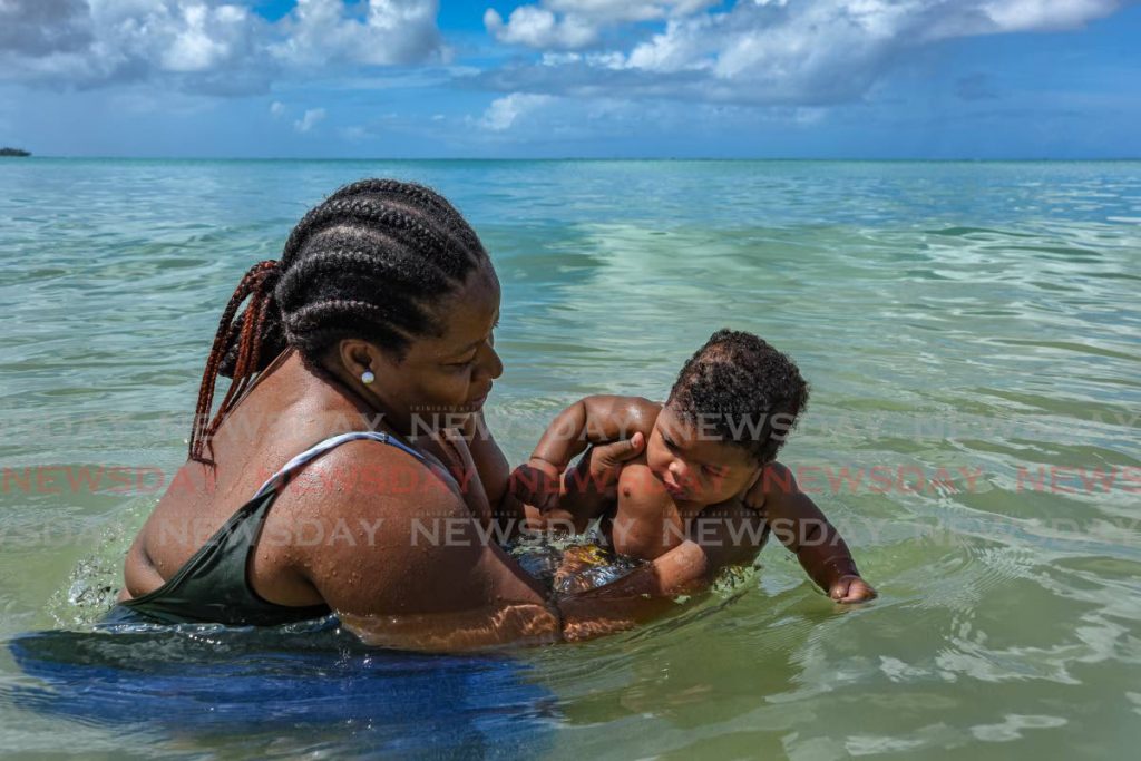 Rennee Sampson dips her six-month-old baby Kymani Phillips into the water at Buccoo Bay, Tobago, on Saturday. PHOTO BY AYANNA KINSALE -  