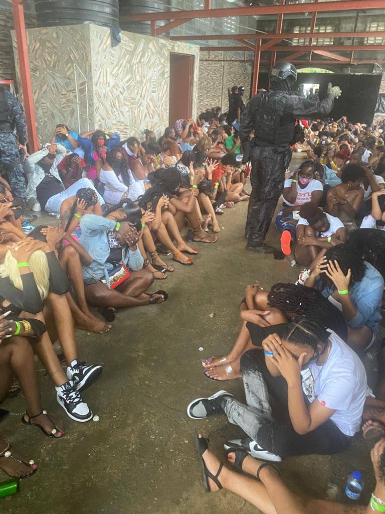 PARTY DONE: Partygoers sit in the ground in a private residence in Kelly Village, Caroni after police raided a “zesser” party on Sunday morning, with 250 people being charged later for breaching covid19 public health regulations.  - ttps