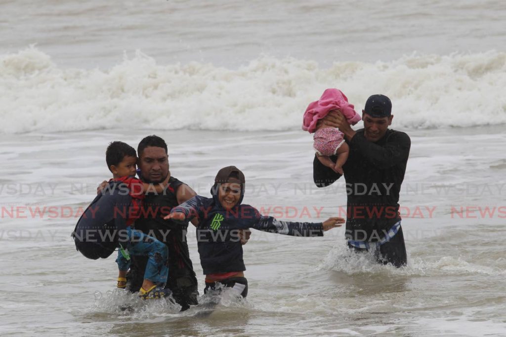 BABE IN ARMS:
A man keeps a baby well above the waves as he and other migrants believed to be Venezuelans landed at Los Iros beach after arriving in a pirogue. PHOTO BY LINCOLN HOLDER - 