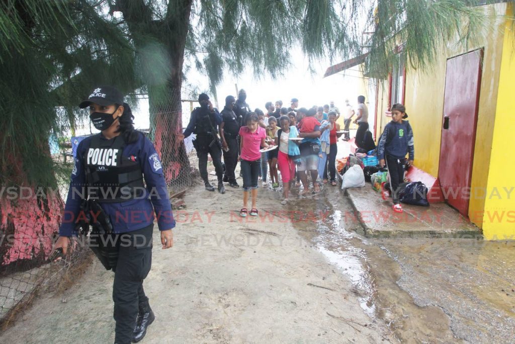 A policewoman escorts Venezuelans who arrived on pirogues at Los Iros, Erin on Tuesday. The group numbering 26 have since been placed in the state quarantine facility at the heliport in Chaguaramas. Three of them were released in the care of relatives but the majority remain at the heliport. On Saturday attorneys in related cases were seeking the court's intervention on the status of their Venezuelan clients. In one instance, a judge halted the deportation of 19 Venezuelans. PHOTO BY LINCOLN HOLDER - 