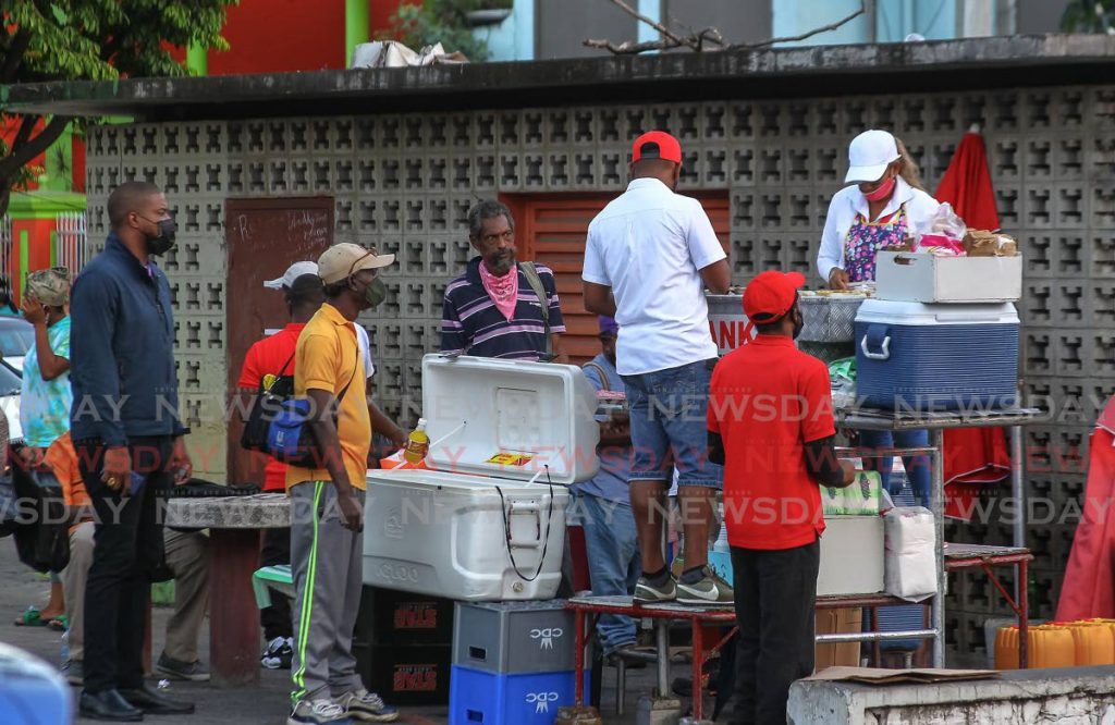 Customers dressed in their “fineries” wait for their orders from Pank’s Doubles on the Brian Lara Promenade in Port of Spain, Wednesday. - ROGER JACOB