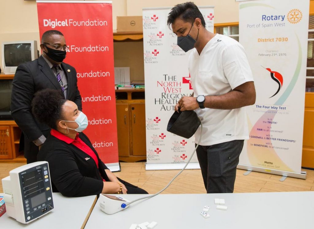 Digicel Foundation project co-ordinator Lynelle Callender, seated, gets her blood pressure  checked by head nurse Kabir Ramanan using the new vital sign monitor. Looking on is Garth Sobers of  Rotary Club PoS West. - 