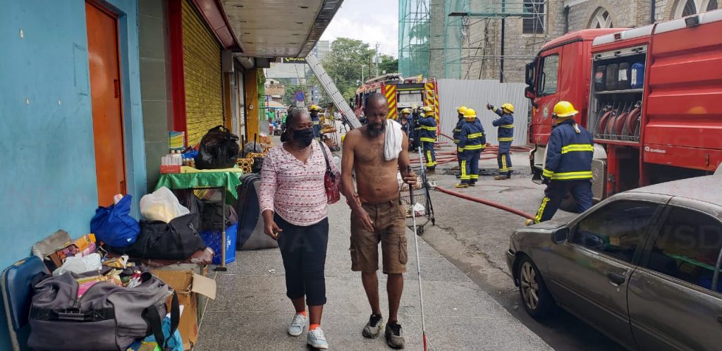 East Port of Spain resident Angelo Joseph and another resident walk away from a fire on Independence Square, Tuesday afternoon. Photo by Roger Jacob