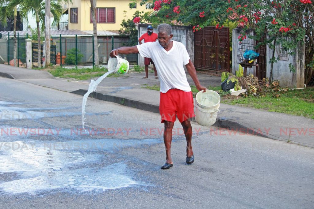 A resident throws a combination of water and bleach onto the road to wash away the blood where Trevor Hospedales was murdered on Sunday afternoon in Santa Flora in broad daylight. - CHEQUANA WHEELER