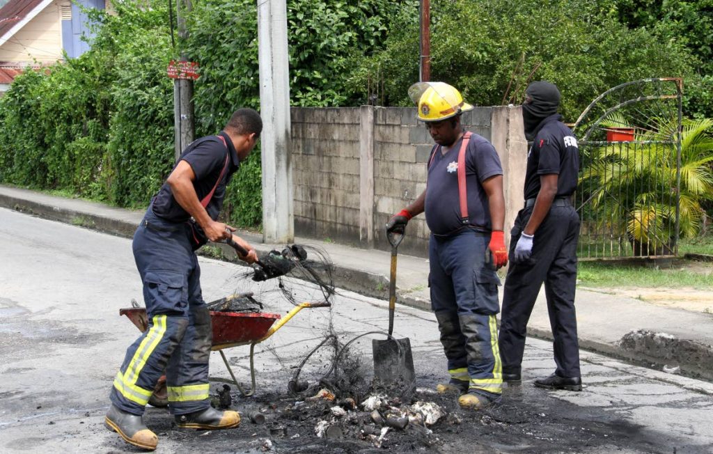 Police officers secure the area where burning debris was set ablaze by residents at the corner of Blackford Street and Cantaro Ext Road, Santa Cruz on Sunday. Residents were protesting the police killing of Shaquille Charles, 25.  - Angelo Marcelle