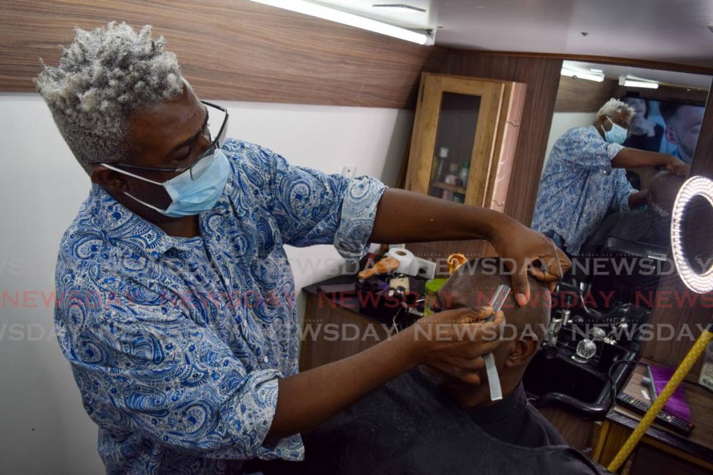 Nyron Charles, owner of Tending and Stylin Mobile Barbering Services, shaves the hairline of customer Sheldon Cumberbatch in his mobile barbering unit. The self-employed cannot be included in the National Insurance Scheme because it would be too costly, Finance Minister Colm Imbert told the Senate last Tuesday. File photo - 