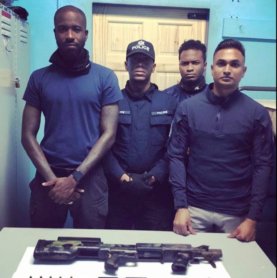 Officers of the North Eastern Division Task Force stand near a semi-automatic shotgun, a pistol and 16 rounds of ammunition seized during a raid at a house in Morvant. 

PHOTO COURTESY TTPS - TTPS