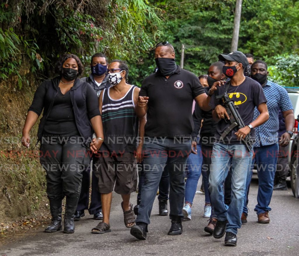 Father of Andrea Bharatt, Randolph Bharatt, centre, is escorted by police officers at the Heights of Aripo where Andrea's body was found.  - AYANNA KINSALE