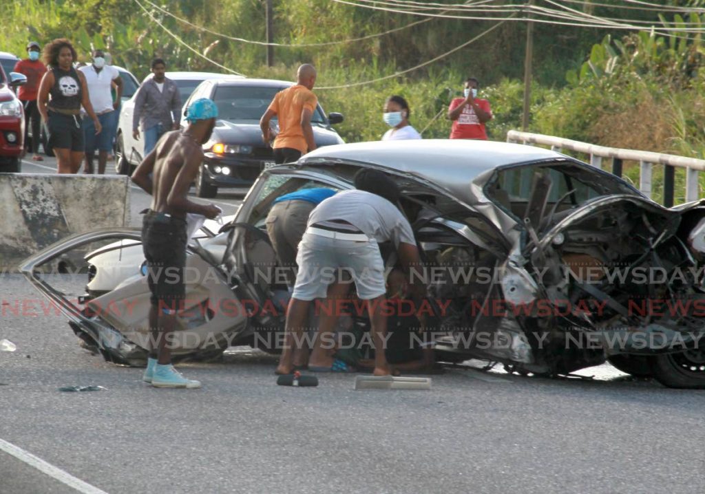 MANGLED: People try to assist the driver of this Nissan Almera after it crashed into a concrete divider on the east-bound side of the Churchill Roosevelt Highway in Arima on Sunday afternoon. PHOTO BY ROGER JACOB - 