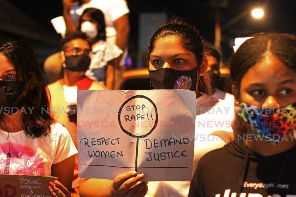 Women hold placards with messages during a candlelight vigil held by the Concerned Citizens of Chaguanas and Environs outside the Chaguanas Market on Tuesday night. PHOTOS BY MARVIN HAMILTON - 