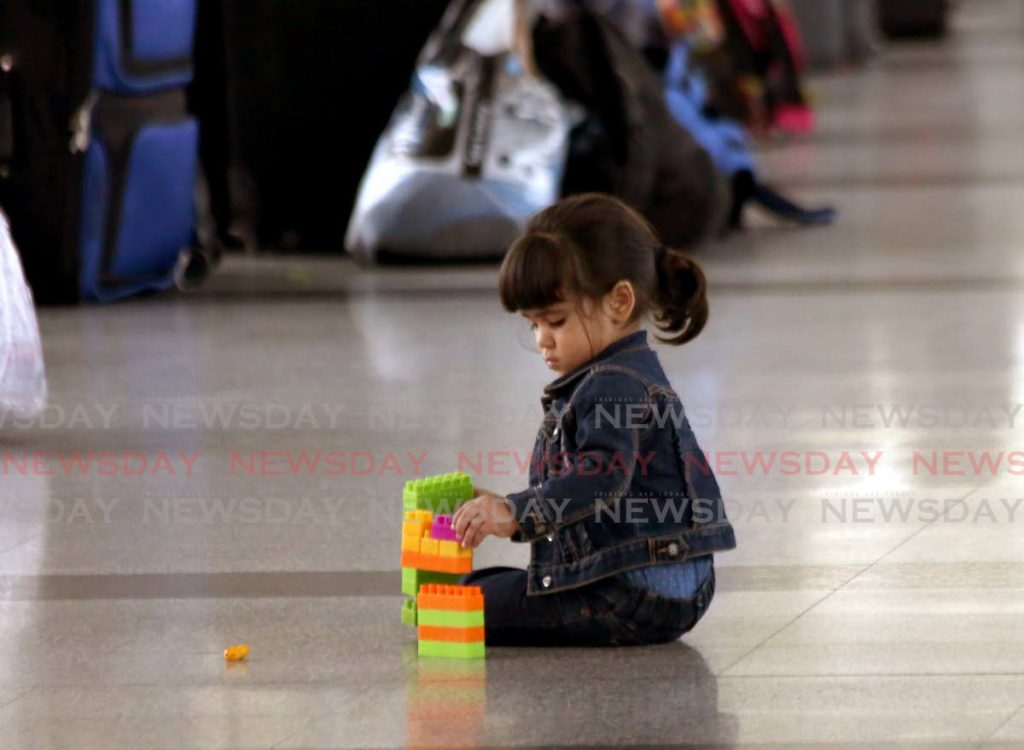 Una niña juega con sus juguetes mientras espera con sus padres en el aeropuerto de Piarco para abordar un vuelo de regreso a Venezuela - Sureash Cholai