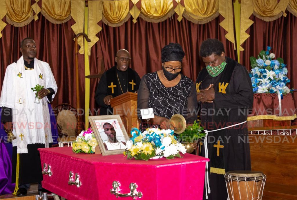 A Mother of the Mt Paran Spiritual Baptist Church rings the bell as she performs the last rites at the funeral of Isaiah Thomas on Monday in Bethel. At left is Thomas's uncle Barrington 