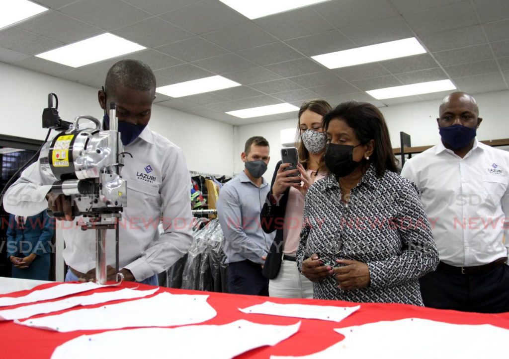 Dwain West shows Minister of Trade and Industry Paula Gopee-Scoon how the straight blade cutter works during a tour at Lazuri Apparel, San Juan on Wednesday. At right is CEO Roger Roach, while TTMA president Franka Costelloe records the moment on her phone. - 