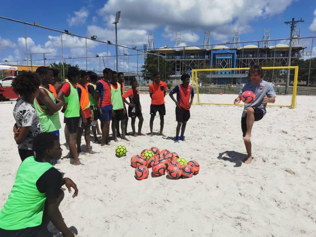 National beach soccer coach Ramiro Amarelle, right, demonstrates some skill for members of the Boys and Girls Club at a recent clinic. 
 - TTFA Media