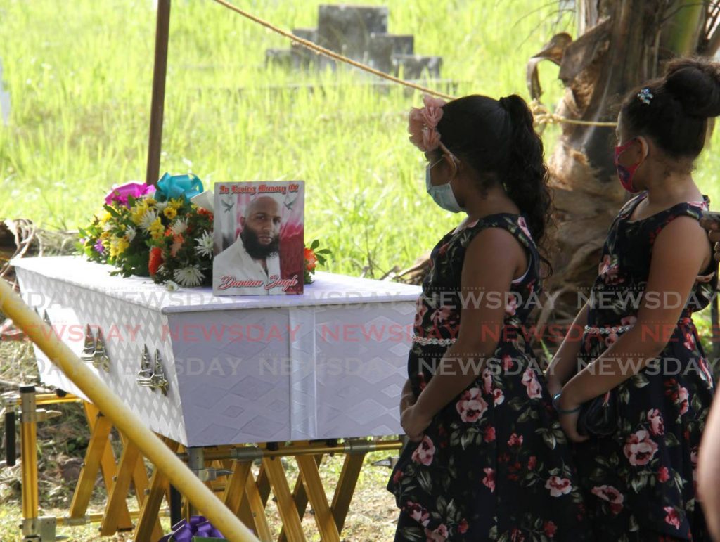 Kelsey Singh, left, looks at a photo of her father Damian Singh during his funeral at the Tableland Public Cemetery on Tuesday. Singh died from the covid19 virus on Sunday.  - Photo by Ayanna Kinsale