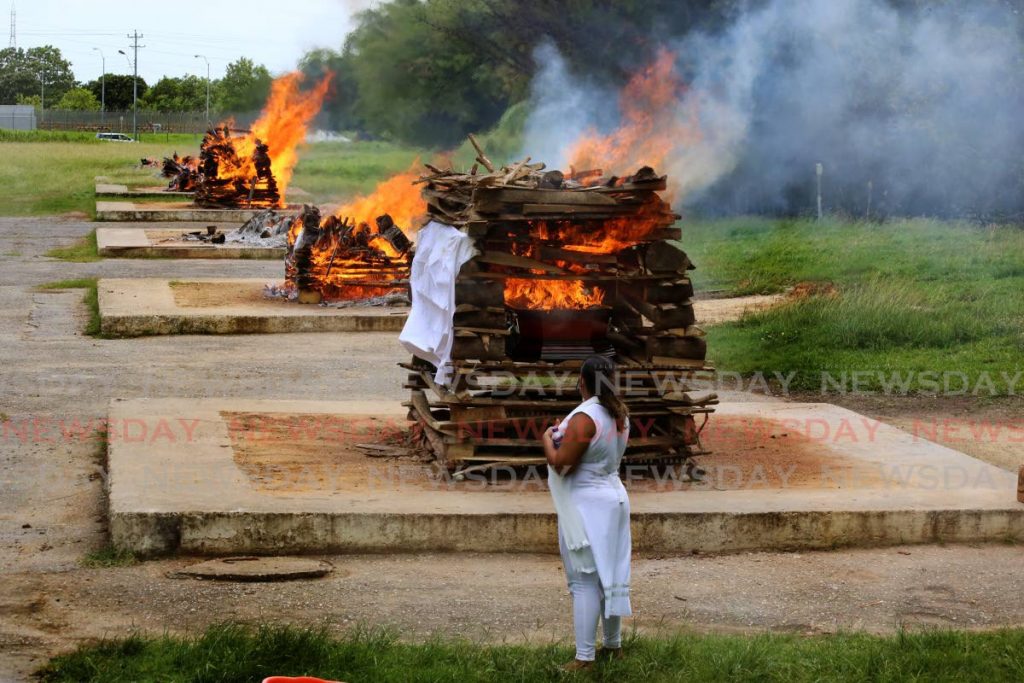 STARK REALITY: 
A woman looks at the burning pyre of a relative whose cremation, along with eight others, happened at the Caroni cremation site on Wednesday. Public health regulations because of covid19 limits the number of mourners at a funeral to five. - SUREASH CHOLAI