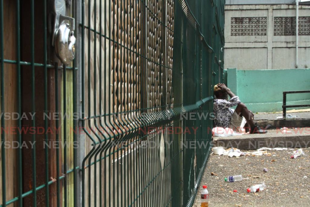 STILL LOCKED: A man sits outside the locked temporary shelter at Riverside Plaza in East Port of Spain on Sunday. The mayor has refused to open the shelter since the NGO who will manage its use has an ongoing court matter with the corporation. Photo by Marvin Hamilton