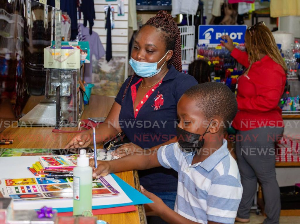 Dredon Roachford, 9, writes on a sticker book while shoping with his mother Nadia Hurdle on Monday at Nelson's Book Store, Ashora Court, Milford Road, Tobago. Hurdle said she was grateful that book stores were allowed to open so she could purchase supplies for her son to do his reading and school projects. - DAVID REID 
