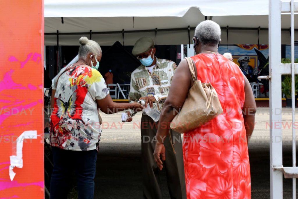 Two women sanitise before entering the paddock area of the Queen's Park Savannah to get the second dose of the covid19 vaccine. Photo by Sureash Cholai - SUREASH CHOLAI