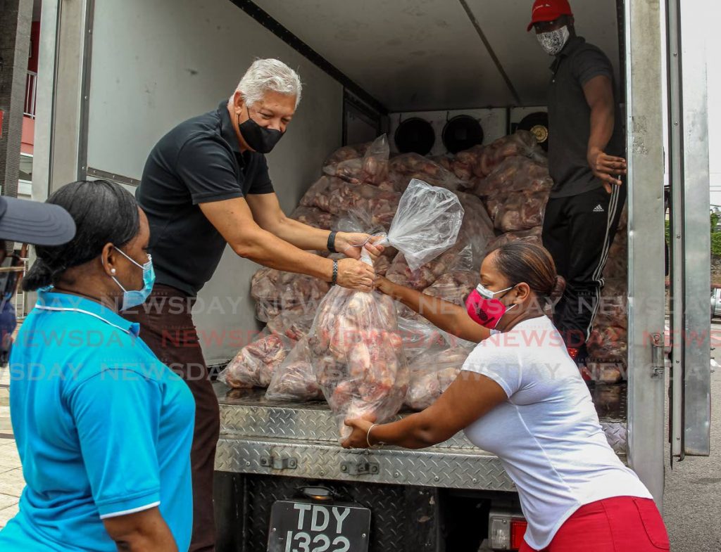 Port of Spain Mayor Joel Martinez, passes a bag of chicken to councillor Nicole Young as councillor Esther Sylvester looks on outside City Hall on Thursday. The chicken was delivered to the corporation by Namdevco. - ROGER JACOB