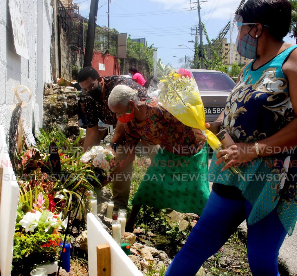 WITH LOVE: Morvant residents place flowers and candles in Second Caledonia on Sunday to mark the one-year death anniversary of three men who were killed by police. PHOTO BY SUREASH CHOLAI 