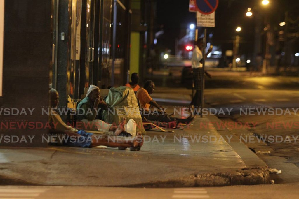 Homeless people rest on the pavement outside a bank in Port of Spain. - Photo by Marvin Hamilton