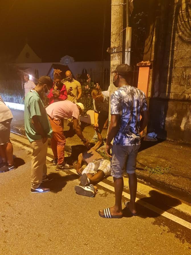 St Ann's residents, including Newsday reporter Andrew Gioannetti, help an injured Brent Hudson who was hit by a van which sped away on Wednesday night. - 