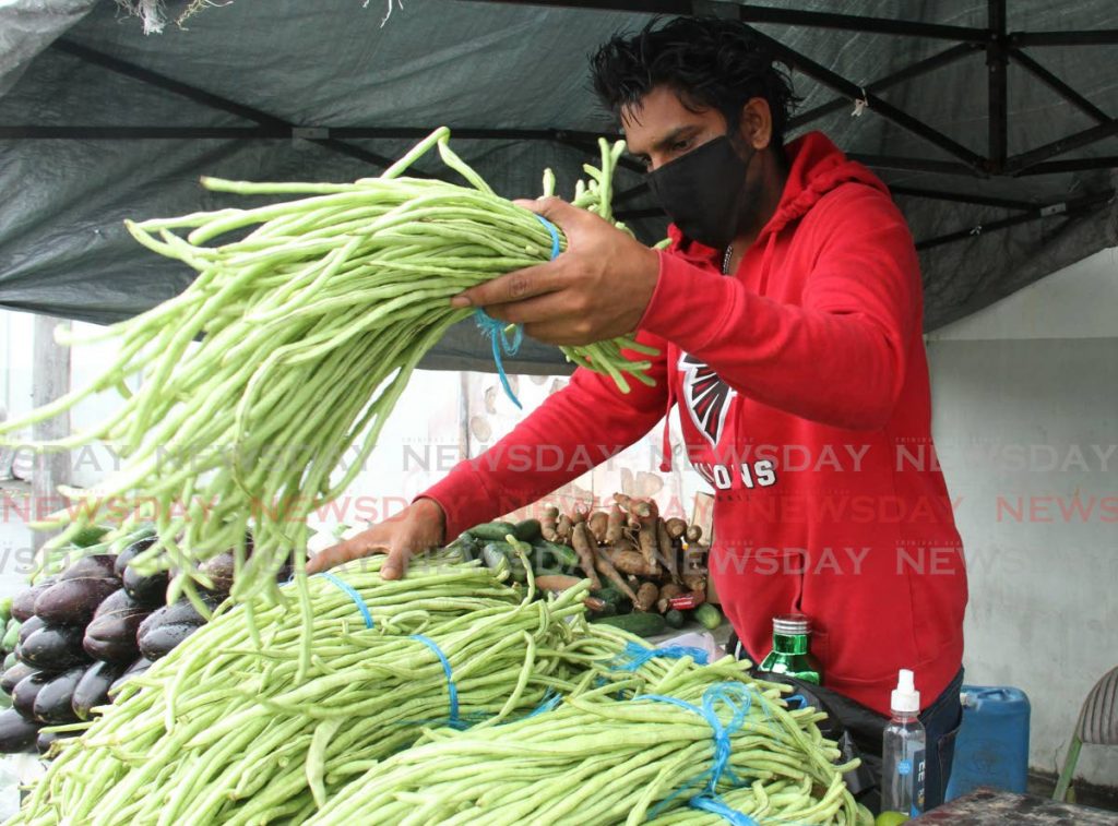 Vendor Brandon Sookhoo sets out bundles of bodi for sale on a table at a stall on Southern Main Road, California, Couva on July 6. - Photo by Ayanna Kinsale