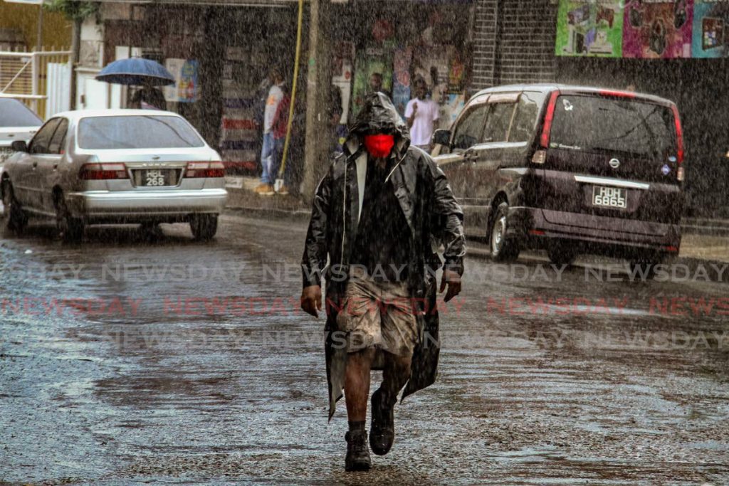 This man walks through the rain with his rain coat on Library Corner, San Fernando. - Photo by Ayanna Kinsale
