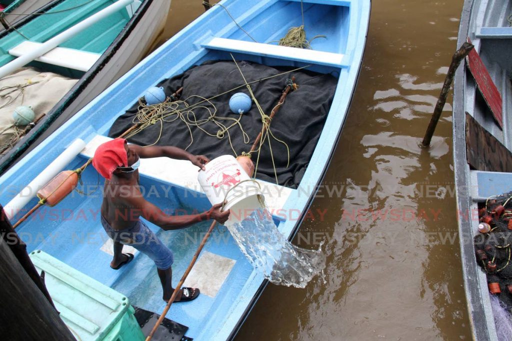 Overnight rain forced fisherman Raymond Montano to bail water from his boat on Wednesday morning at the River of Hope in La Ruffin Village, Moruga. - Photo by Angelo Marcelle