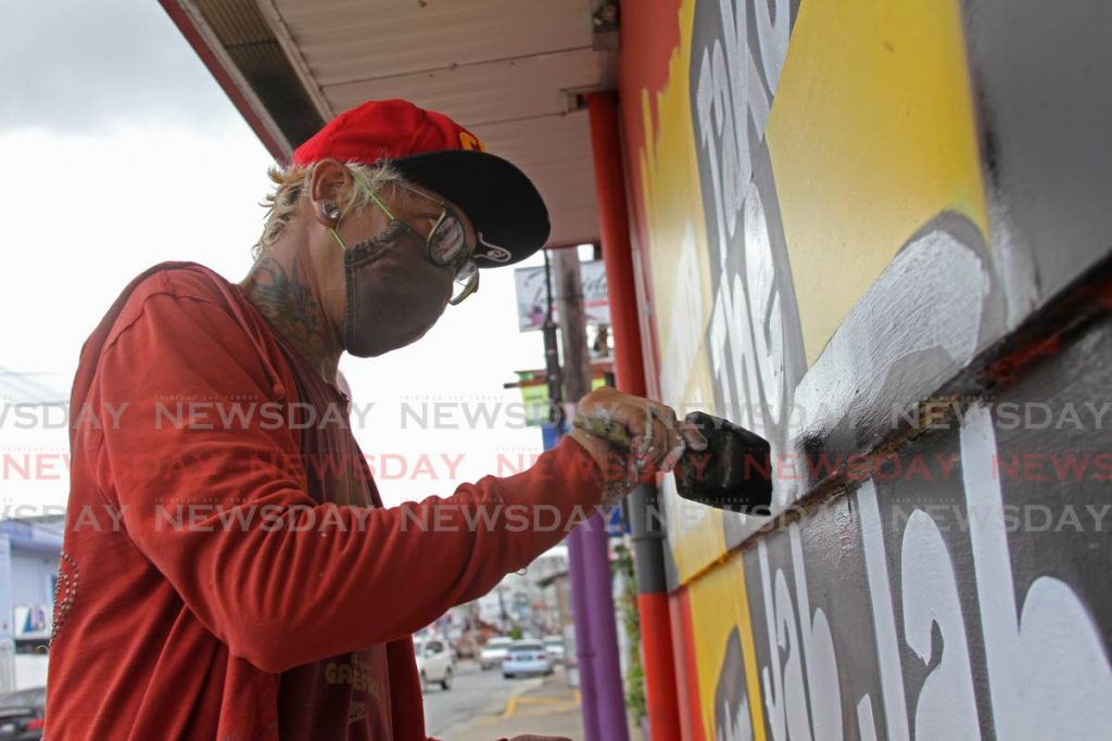 Graffiti artist Zinnia Cheewah puts finishing touches on the Take the Jab Jab mural on the wall of Mario's Pizzeria. Cheewah is also working on a mural with other artists in memory of five men killed by police in Morvant in 2020. - Photo by Marvin Hamilton