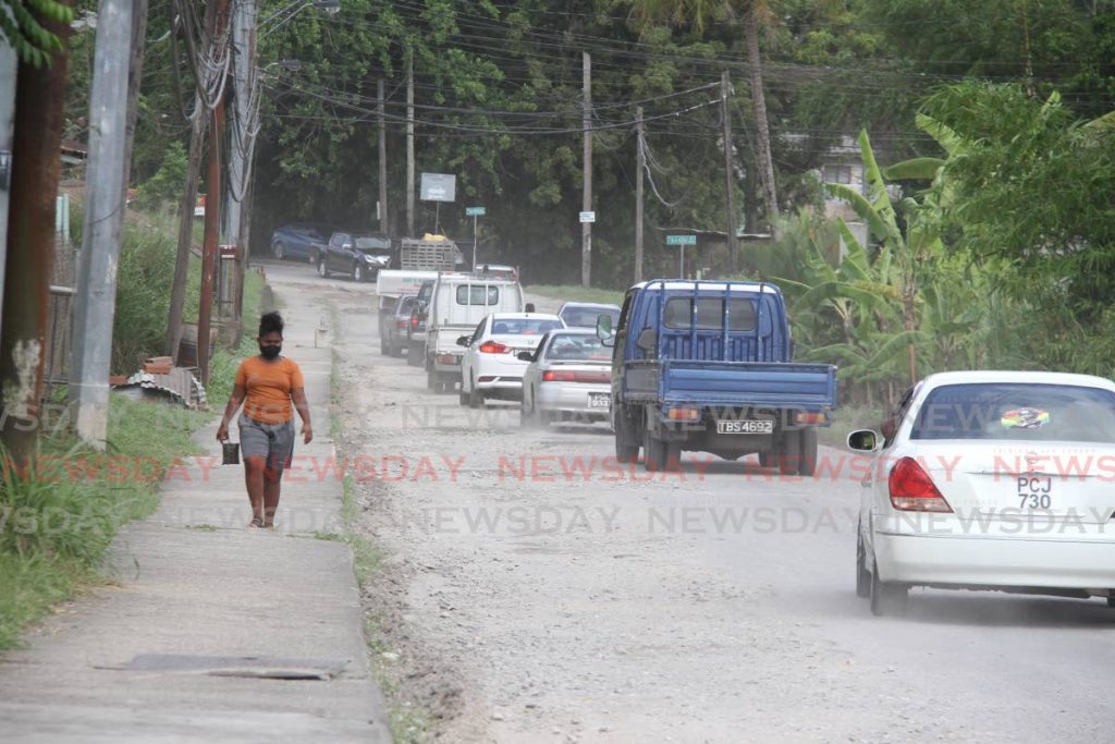 A pedestrian walks through a cloud of dust as drivers do their best to navigate the Guapo/Cap-de-Ville Main Road, Port Fortin, given its state of disrepair on Tuesday. Photo by Angelo Marcelle