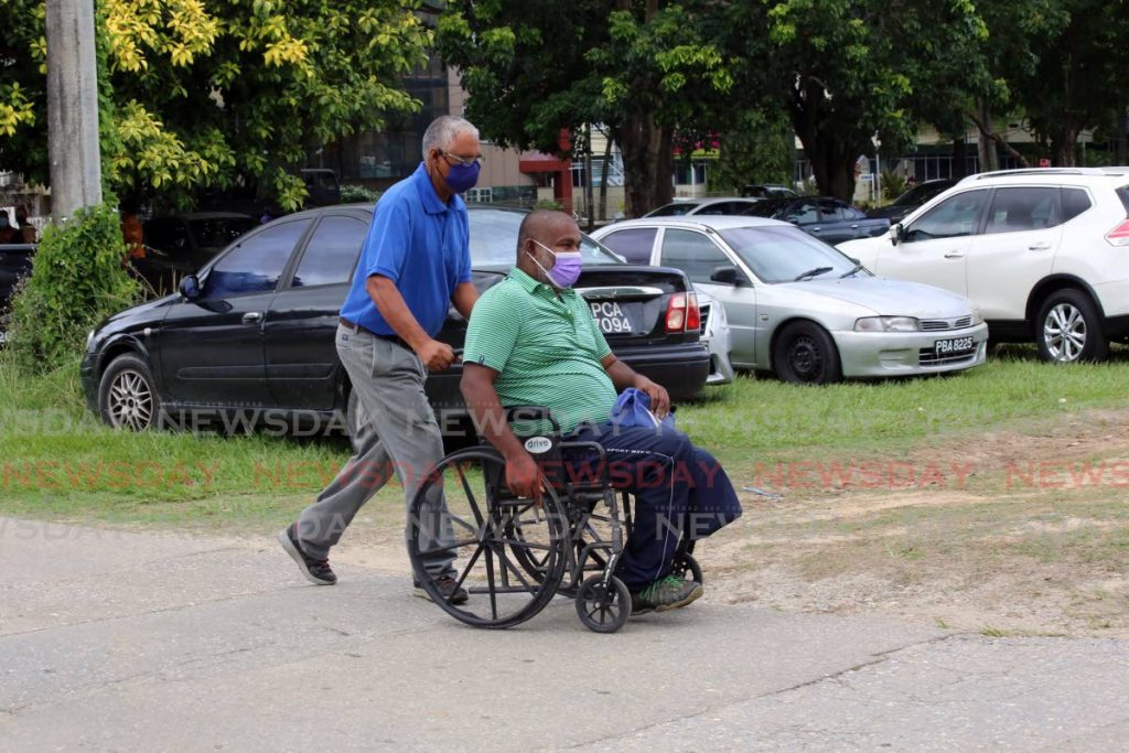 A man guides the wheelchair carrying his relative towards the Paddock of the Queen's Park Savannah, where people with disabilities were specially invited to participate in the mass vaccination drive. Photo by Sureash Cholai