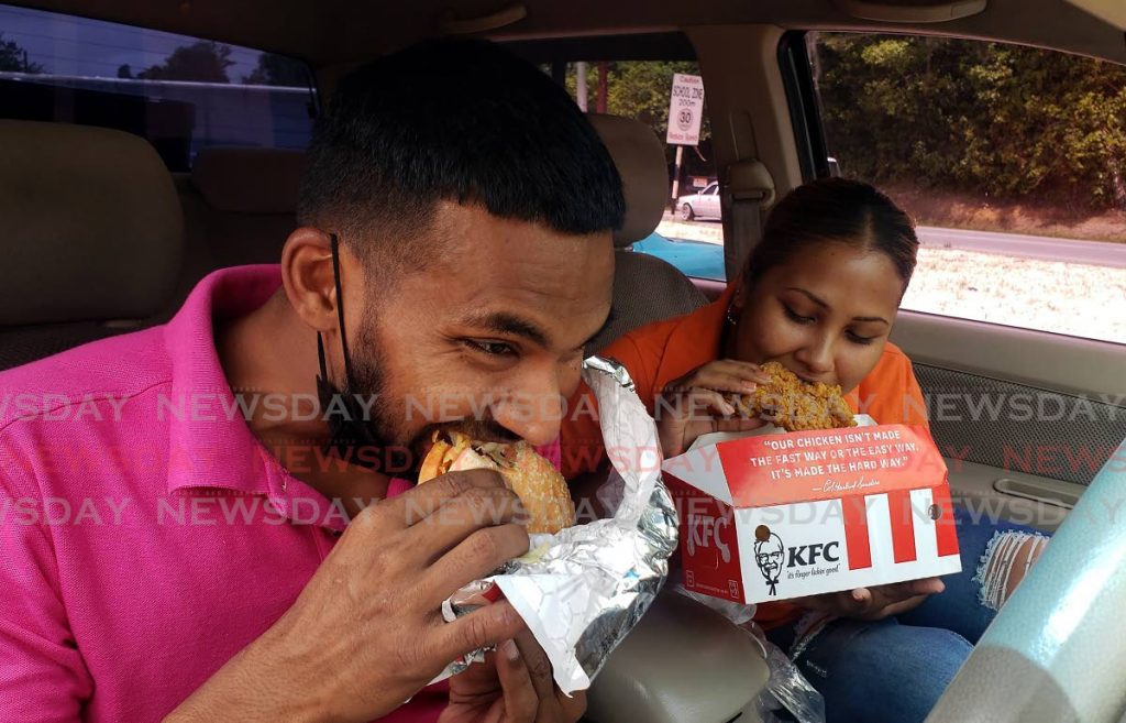 Pritam Persad and his wife Risha chow down on their favorite KFC meal after some restrictions on food businesses were lifted on Monday allowing them to indulge in their favorite fast food at the newly opened KFC location in Guiaco Sangre Grande. - Photo by Roger Jacob