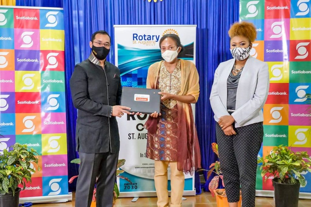 Energy Minister Stuart Young, left, presents a laptop to a representative of one of the schools that received devices donated by the Rotary Club of St Augustine West.  At right is Education Minister Nyan Gadsby Dolly. - 