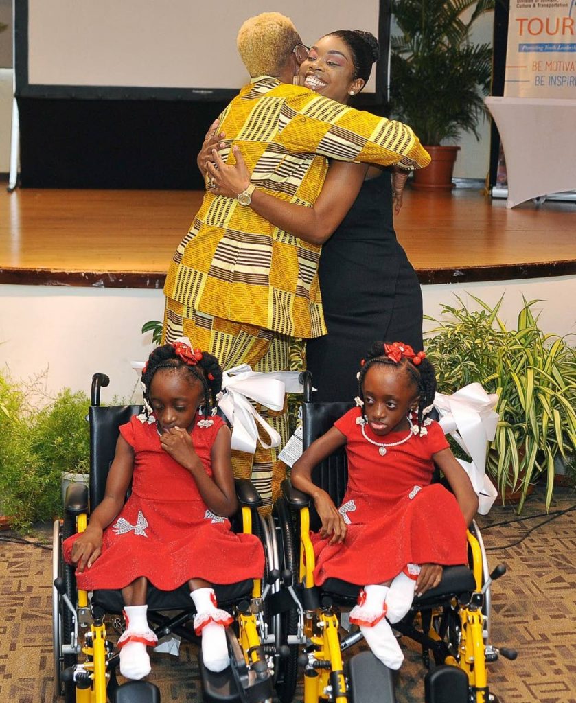 In November 2019, Tourism Secretary Nadine Stewart-Phillips, right, hugs an official as two wheelchairs are presented to twins girls.  - Photo courtesy the Tobago House of Assembly