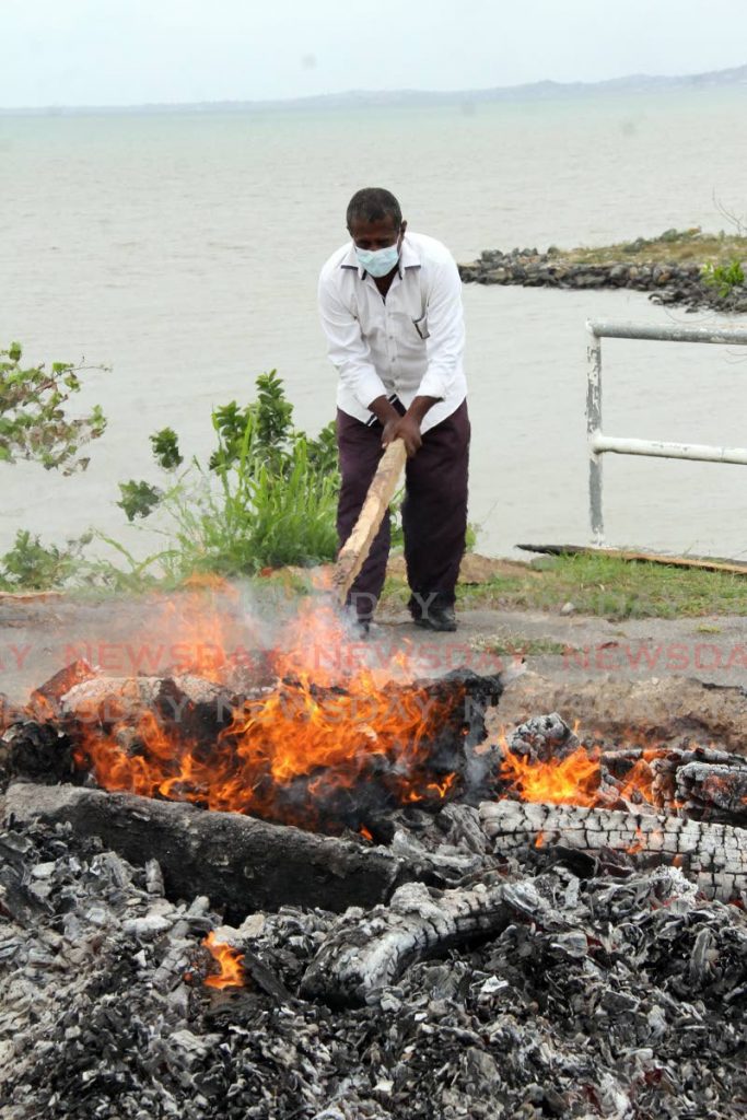 A funeral home employee ensures the fire consumes the contents on a pyre at Shore of Peace cremation site South Oropuche on May 26.  - Photo by Angelo Marcelle