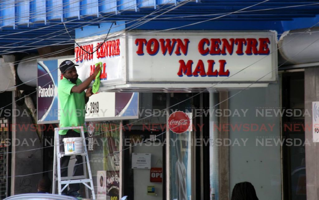 A worker cleans the Town Centre Mall sign on Frederick Street in Port of Spain. - Photo by Sureash Cholai