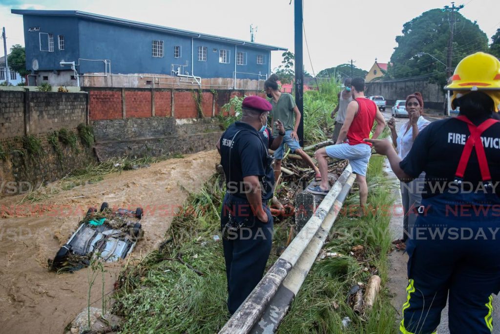 Fire officers and St Ann's residents look at two cars in the St Ann's river which were swept away on Tuesday by flood waters. - Jeff K. Mayers