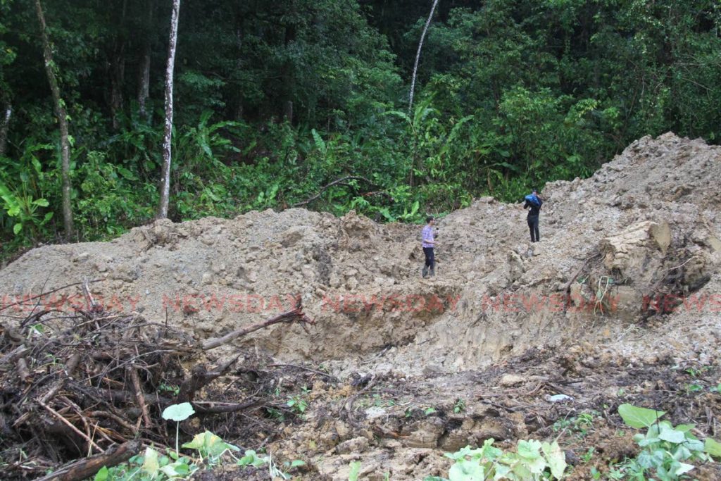 Members of the media look at the hole from which a woman's body was retrieved by police, at Warden Road, Sangre Chiquito on Monday. Police believe the body to be that of Annalisa Gokool who had been reported missing on June 9. - Angelo Marcelle