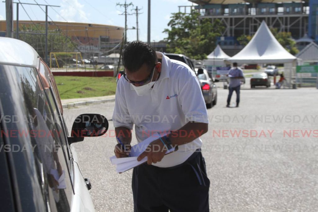 A volunteer screens a driver on a slow day at the Ato Boldon stadium for persons getting jab of either Sinopharm or AstraZeneca in both the drive through and walk-ins on Wednesday. Photo by Marvin Hamilton