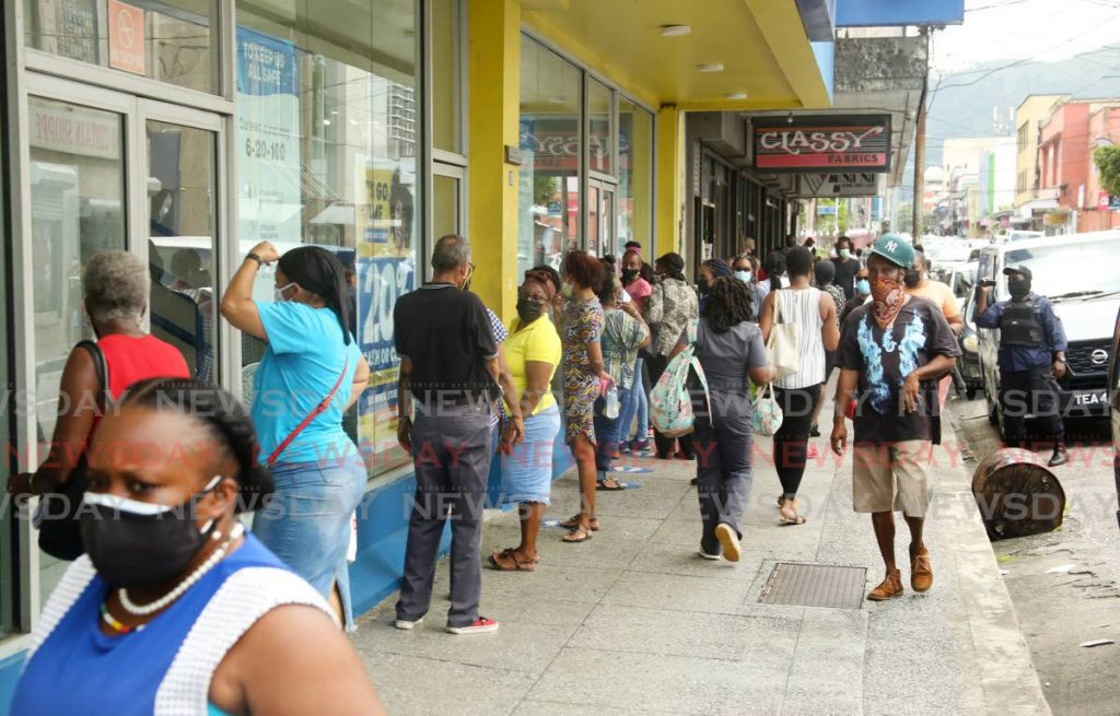 Shoppers line up outside Courts on Frederick Street in Port of Spain as a police officer ensures health protocols are followed. Photo by Sureash Cholai