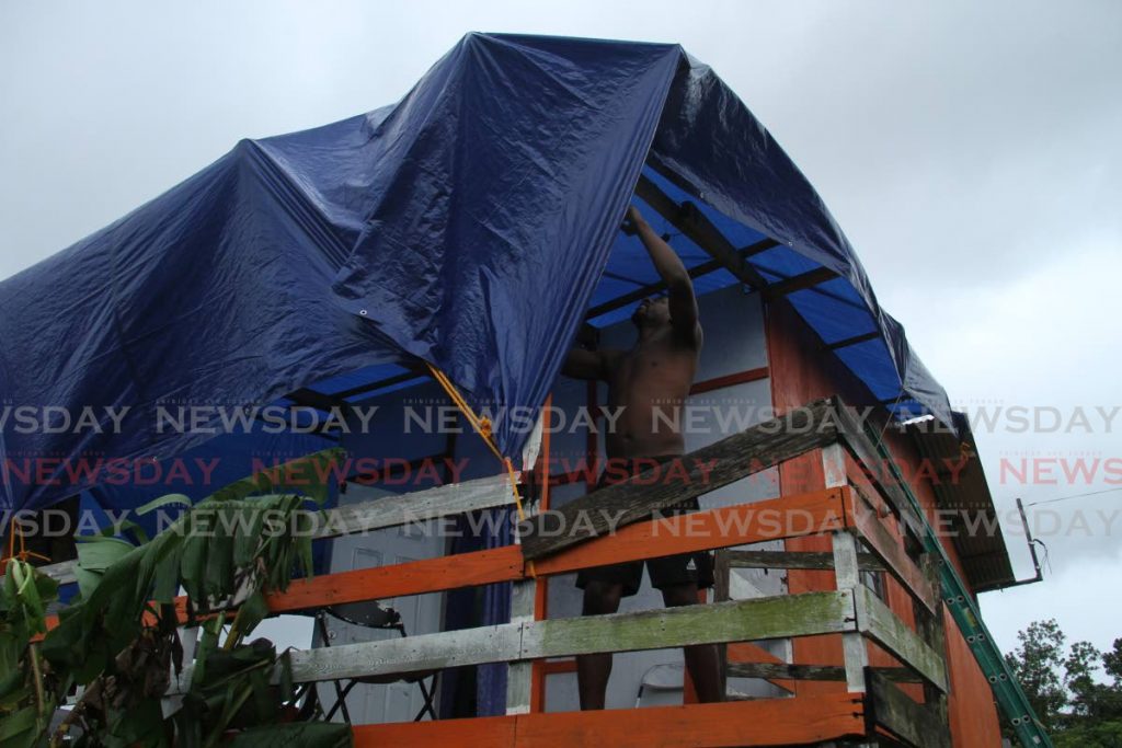 COVERING UP: File photo of Kynu Frederick of Hawk Ave, Warden Rd, Point Fortin tightens a tarpaulin over his house on Friday after his roof was blown off by high winds on Thursday night. - AYANNA KINSALE