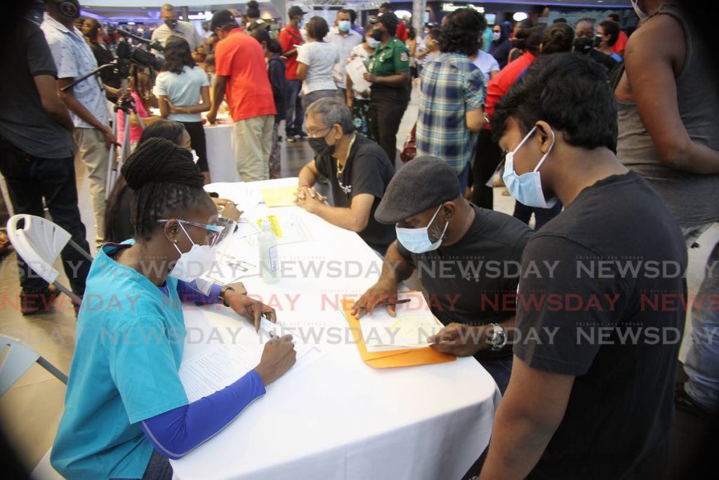 Volunteers register people at a desk for Pfizer vaccines at Gulf City Mall, San Fernando on Saturday. - Photo by Lincoln Holder