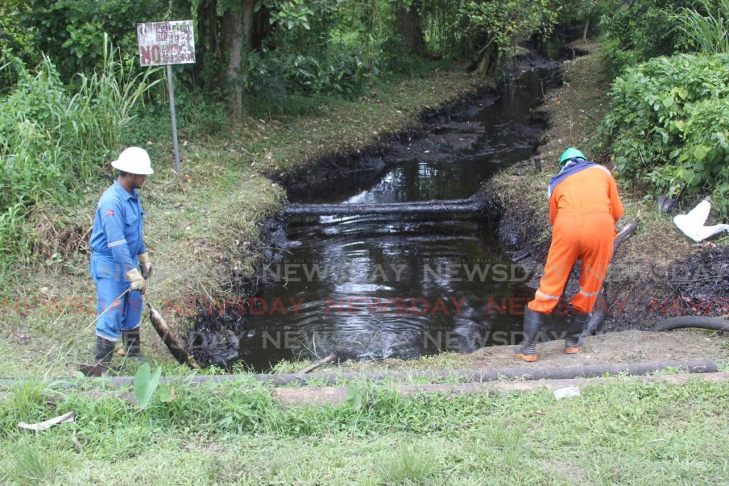 Workers from Quintana services install an oil containment boom in a river in Point Ligoure, Point Fortin following an oil leak. Heritage Petroleum Company Ltd is investigating the source of the leak. - Photo by Lincoln Holder