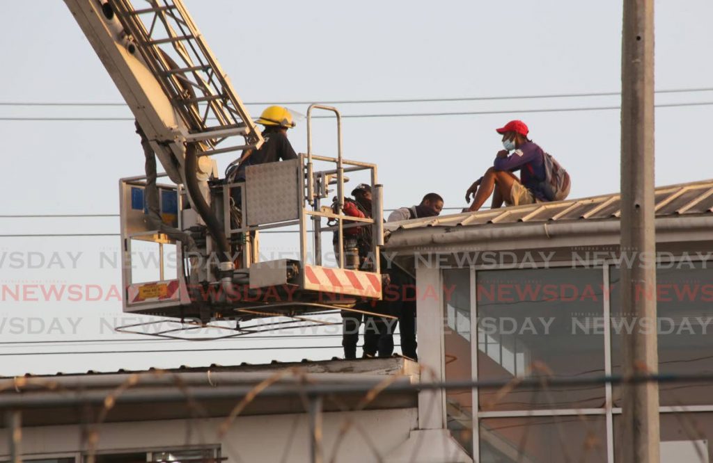 A man (right) who climbed on to the roof of City Gate in Port of Spain with the intention of jumping caught the attention of the a police. With the assistance of  fire service officers, they spent several hours talking him down. Photo by Sureash Cholai 