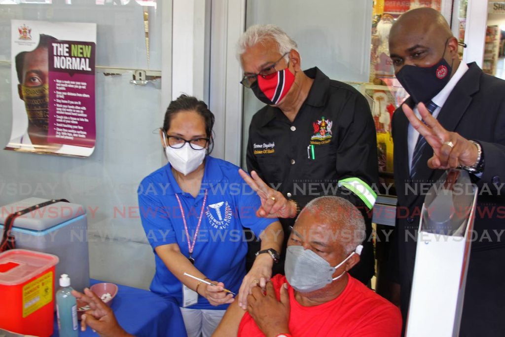 Member of Parliament for San Fernando East Brian Manning and Health Minister Terrance Deyalsingh pose for a photo at the covid19 Vaccination Roadtrip in Marabella on Friday, as a health official gives a jab of Johnson & Johnson vaccine to Derek Matthews-Noel. - Photo by Marvin Hamilton