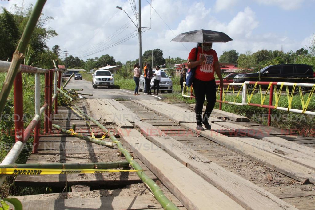 A woman uses the deteriorating bridge on Lightbourne Road, Bonne Aventure, Gasparillo on Wednesday. The bridge has been closed off due to the risk of collapsing. The caution signs, however, were removed and vehicular traffic has since been resumed.  Photo by Marvin Hamilton
